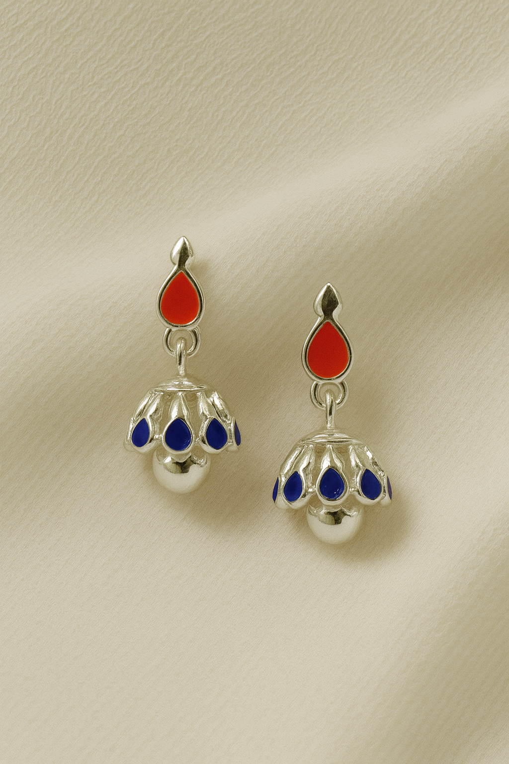Pair of silver earrings with red and blue accents on a beige background
